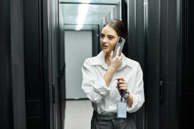Beyaz gömlekli yetenekli bir bilişim uzmanı veri merkezinde bir telefon görüşmesi yapıyor..