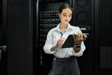 A woman in a white shirt diligently works in a sleek server room, engaging with technology. clipart