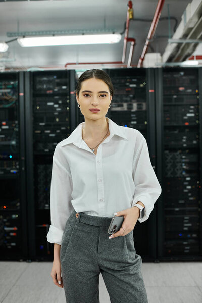 Woman in a white shirt works confidently in a modern server room, managing digital systems.