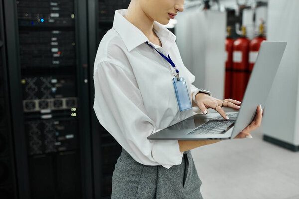 Выделенный ИТ-эксперт в белой рубашке работает с ноутбуком среди продвинутого серверного оборудования.