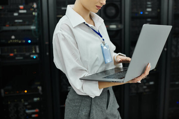 Профессиональная женщина в белой рубашке работает на ноутбуке в шумной серверной.