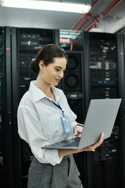 ИТ-специалист в белой рубашке взаимодействует с ноутбуком среди серверного оборудования в дата-центре.