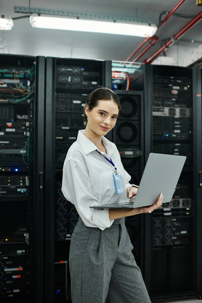 Женщина в белой рубашке эффективно работает над ноутбуком в сложной серверной комнате.