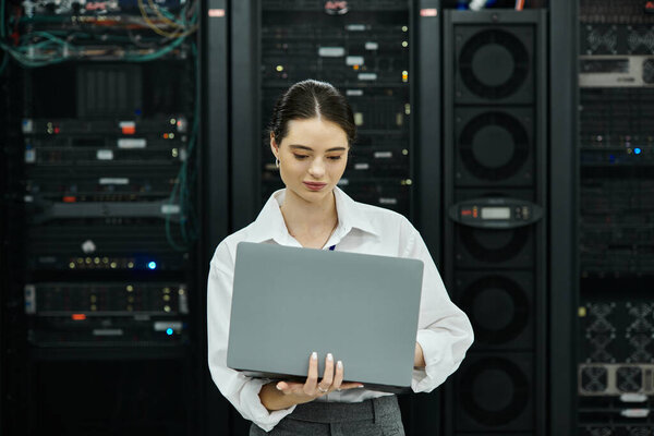 ИТ-специалист в белой рубашке работает на ноутбуке посреди серверных стеллажей в дата-центре.