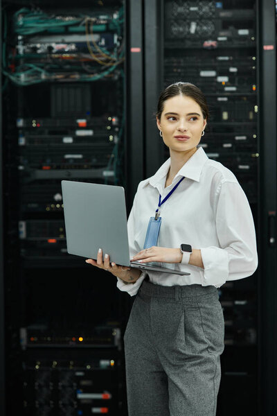 Женщина в белой рубашке работает на ноутбуке в современной серверной, обеспечивая безопасность.