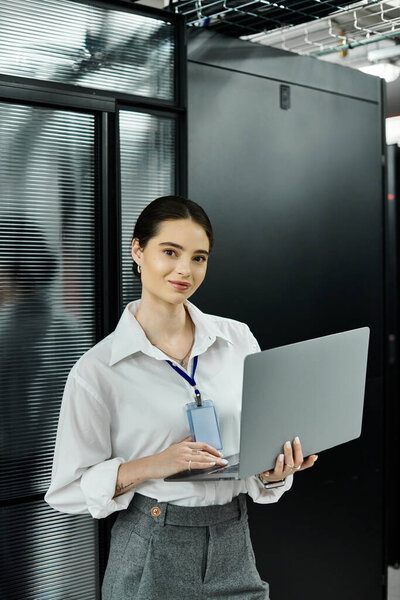 A woman in a white shirt concentrates on her laptop in a high-tech server room.