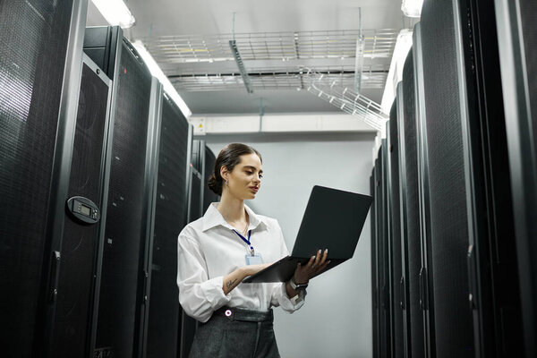 Женщина в белой рубашке усердно работает с ноутбуком в высокотехнологичной серверной.