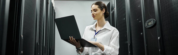 Опытная женщина в белой рубашке работает на ноутбуке посреди серверных стеллажей в дата-центре, баннер
