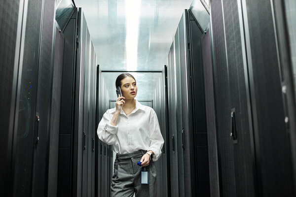 An IT specialist wearing a white shirt is engaged in work inside a sleek server room.