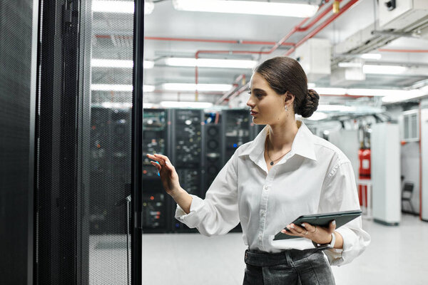 A skilled woman in a white shirt works in a modern server room, overseeing systems.