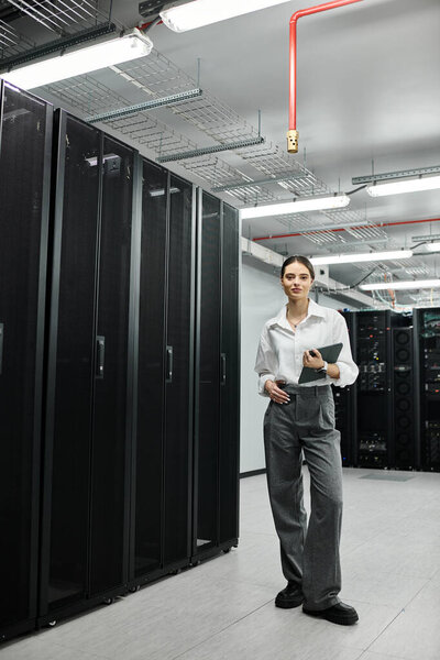A skilled woman in a white shirt checks systems while managing server hardware in a tech hub.