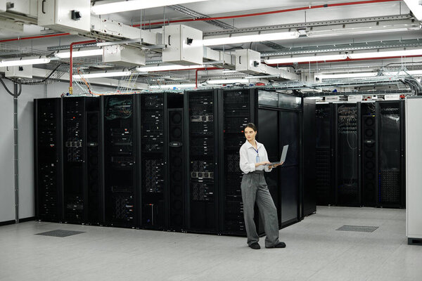 In a modern server room, a woman in a white shirt manages computer systems with focus and skill.