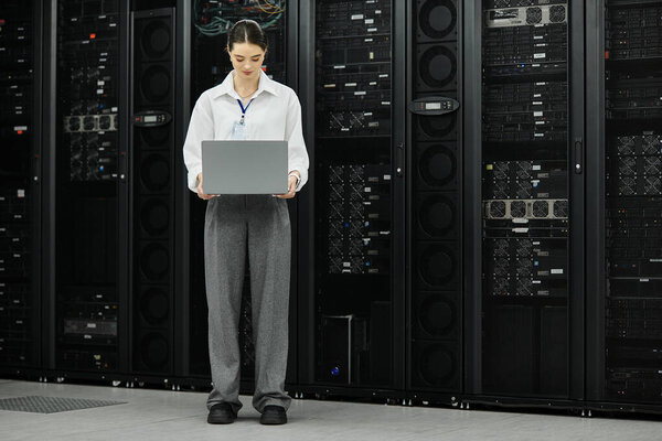 Женщина в белой рубашке работает с ноутбуком, обеспечивая бесперебойную работу в серверной.