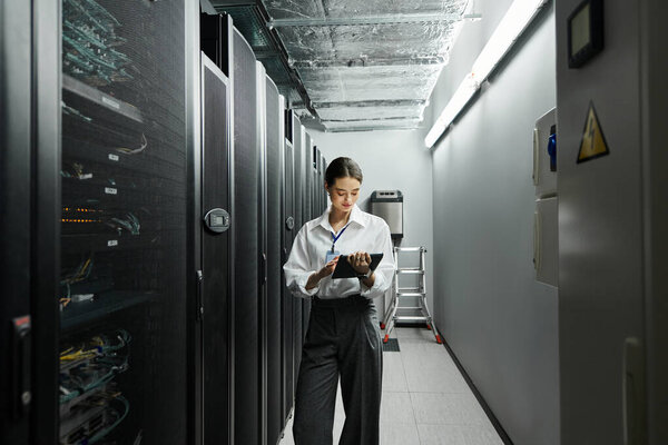 IT specialist in a white shirt focuses on her tasks in a sleek server room with advanced technology.