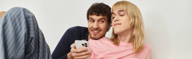 Couple smiles and laughs on the couch, enjoying a show together on their phone. clipart