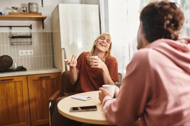 İki mutlu adam, mutfaklarında kahve içerken sıcak bir kahkahayı paylaşıyor..
