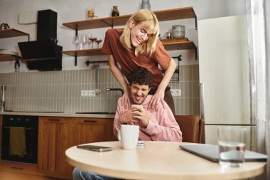 İki adam, şık bir mutfakta kahkaha ve sıcaklığı paylaşırken, aynı zamanda birbirlerine eşlik ederler..