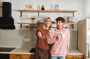 Parlak bir mutfakta telefonlarına bakarken iki adam sıcak bir anın tadını çıkarıyor..