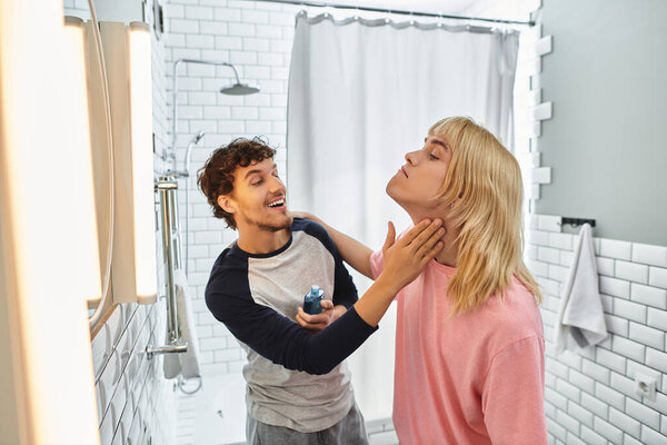 Двое мужчин игриво взаимодействуют в современной ванной комнате, как один стилей другие волосы для специальной прогулки.