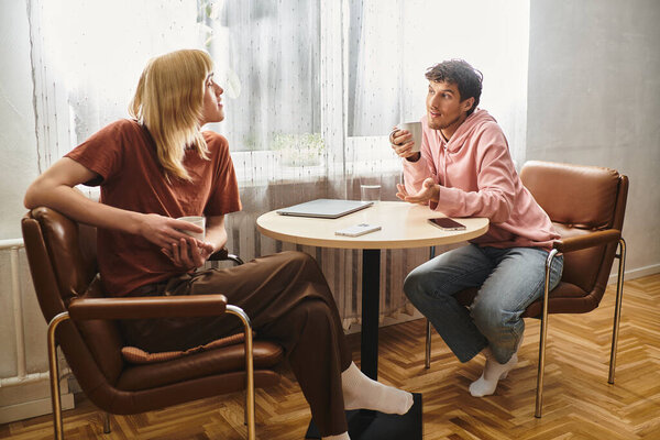Two men engage in a heartfelt conversation while sipping beverages in a sunlit room.