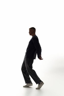 Genç bir adam dinamik dans yeteneklerini minimalist bir arka plana karşı sergiliyor, zarafeti somutlaştırıyor..