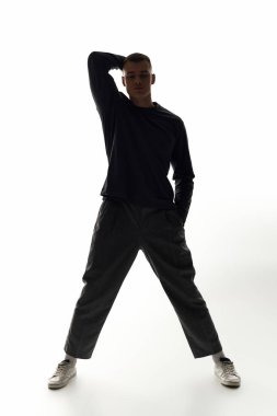 Genç bir adam, parlak bir arka planda vurgulanmış, çarpıcı bir pozda dimdik ayakta duruyor..