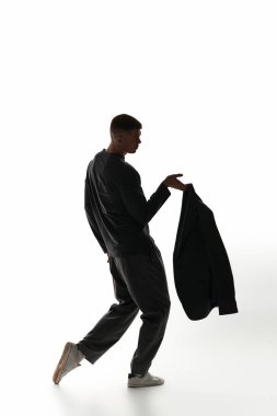 A fashionable young man strikes a dynamic pose while holding a jacket, exuding confidence and style. clipart