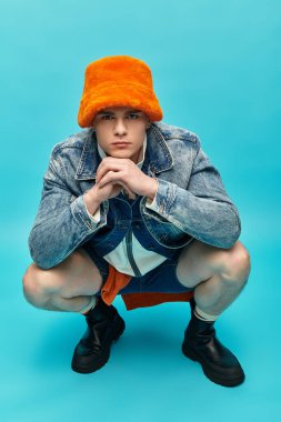 Genç bir adam kendine güveni tam bir şekilde şık kıyafetler içinde parlak turuncu bir şapkası var..