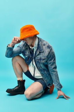 A stylish young man kneels in confidence, dressed in casual summer attire with a vibrant hat. clipart