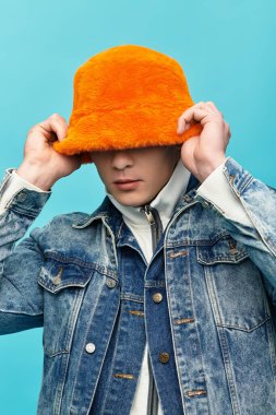 Turuncu şapka takan genç bir adam, neşeli poz verirken moda tarzını sergiliyor..