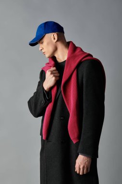 Şık şapkası ve atkısı olan genç bir adam stüdyoda çağdaş bir moda ifadesi sergiliyor..