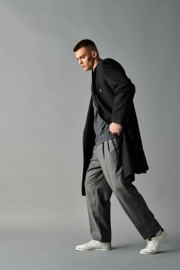 Genç bir adam kasıtlı olarak modern bir mekanda adım atar, stil ve özgüvenin bir karışımını sergiler..