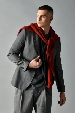Şık bir genç adam, omuzlarına atkı sarılmış şık bir kıyafetle özgüvenle poz verir..