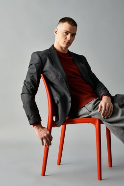 Çekici ve stili olan genç bir adam parlak kırmızı bir sandalyede oturuyor, modern moda sergiliyor..