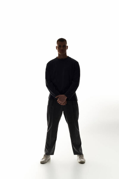 A young man stands firmly with arms crossed, exuding confidence in a sleek, minimalist setting.