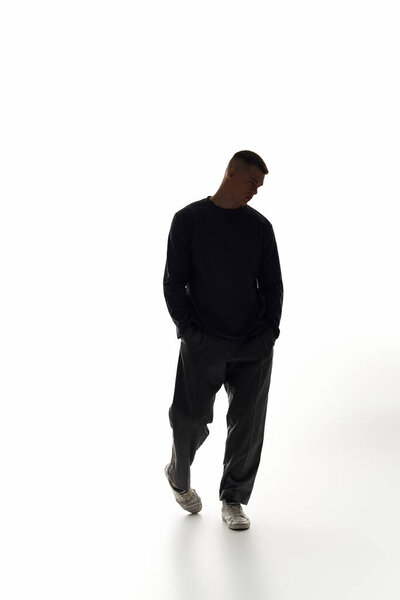 A young, stylish man strolls with relaxed confidence in a bright, minimalistic setting.