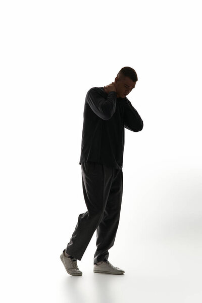 A handsome young man stands alone, lost in thought and introspection, in a softly lit space.