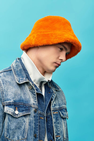 A young man shows off modern style in a denim jacket and orange bucket hat.