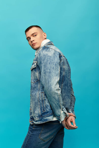 Молодой человек стоит на ярком синем фоне, демонстрируя повседневную и модную джинсовую одежду.