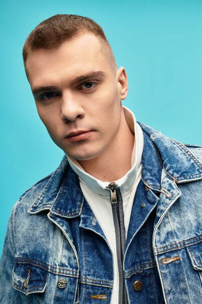 Молодой человек уверенно позирует в джинсовой куртке на ярком синем фоне.