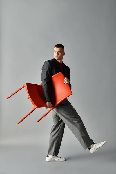 Молодой человек одет стильно ходит с красным стулом, удерживаемым в современной студии.