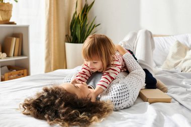 Kıvırcık saçlı anne ve kızı yatakta birlikte oynadıkları eğlenceli anları paylaşıyorlar..