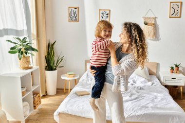 Kıvırcık bir anne, neşeli bir şekilde kızını şık bir odada kaldırır ve aile sevgisini kutlar..