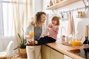 Anne ve kızı, güneşli bir mutfakta taze meyve suyu içerken gülüp kaynaşıyorlar..