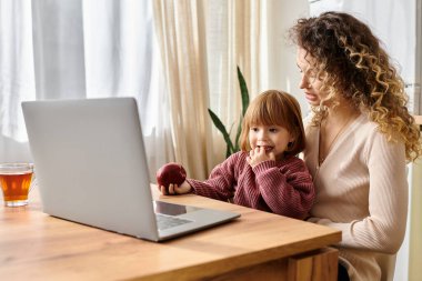Kıvırcık saçlı anne ve kızı evde atıştırmalık yerken keyifli bir anı paylaşıyorlar.