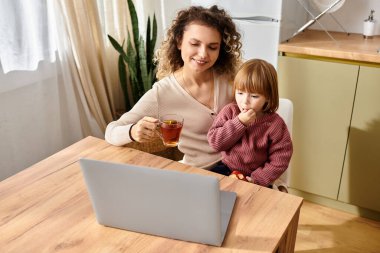 Bir anne ve kızı laptopta bir şey izlerken neşeyle çay yudumluyorlar..