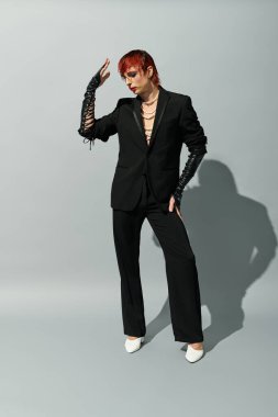 Modaya uygun siyah bir kıyafet giyen genç adam cesur bir duruş sergiliyor..