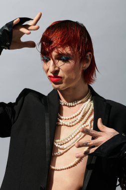 Canlı kızıl saçlı ve kalın makyajlı genç bir adam çarpıcı bir moda gösterisi sunar..