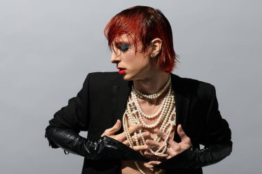 Genç bir adam özgünlüğünü moda ile kucaklar, inciler ve canlı makyajla süslenir..