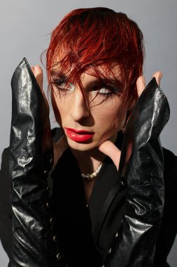 Genç adam canlı kızıl saçlar ve dramatik eldivenlerle tarafsız bir zemine karşı cesur bir stil sergiliyor..